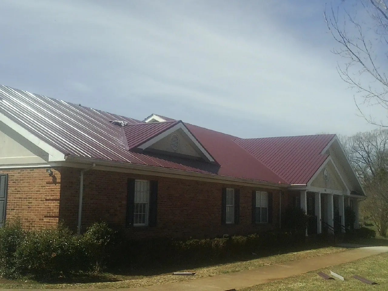 Red metal roof with gabled entries on a long brick building, from a Hail Damage Roof Repair job in Wapwallopen