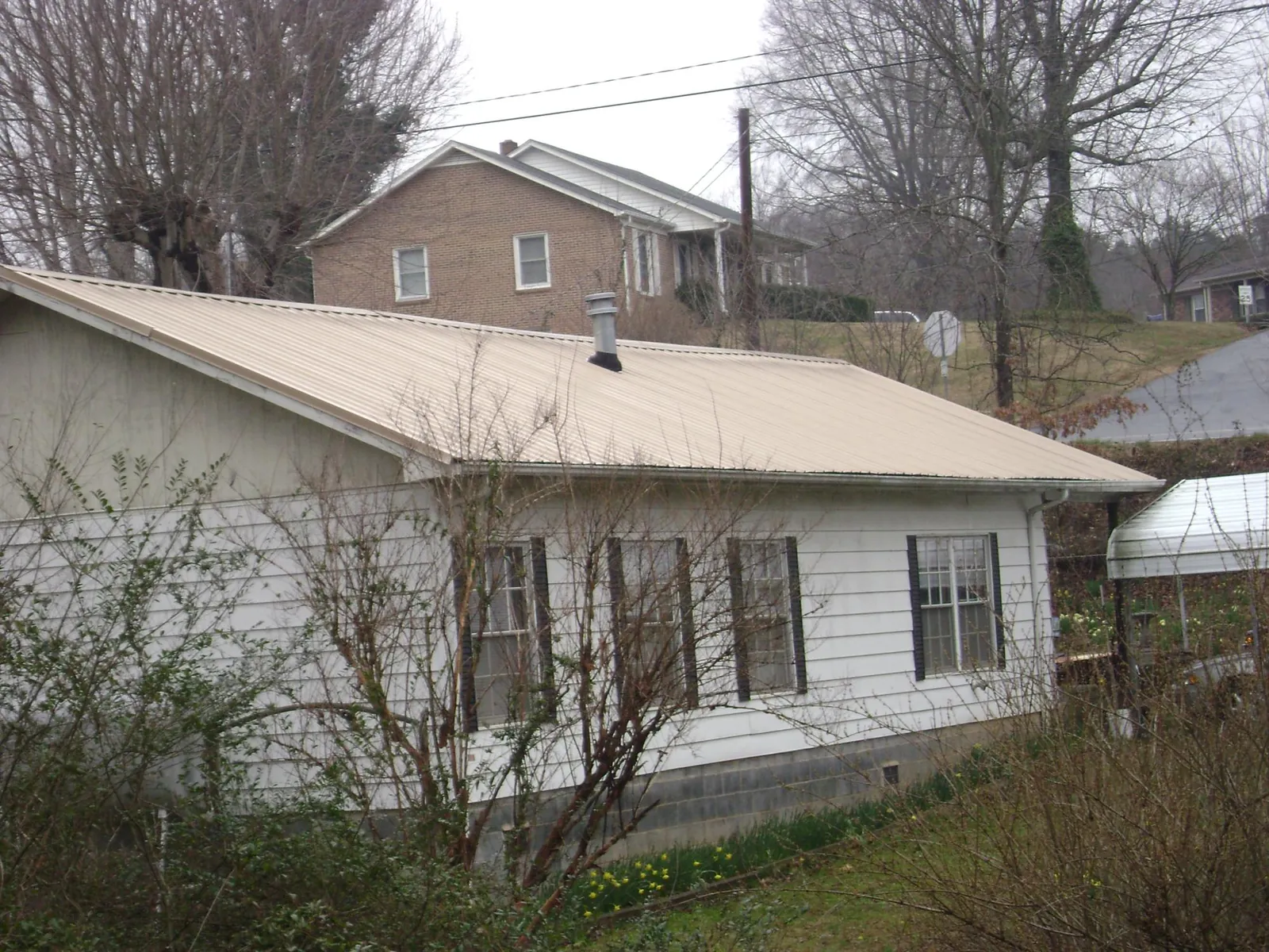 Tan metal roof on a white sided house set into a hillside — Commercial Roofing by Roofing Brothers in Wapwallopen